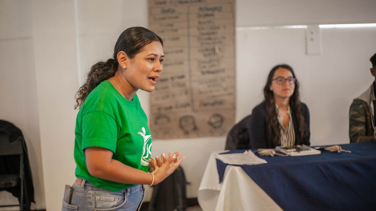 about-01 A young woman passionately speaking during an indoor meeting or workshop.
