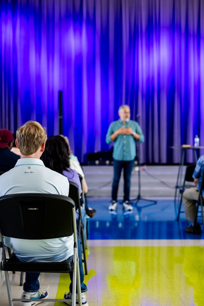 services-02 A speaker addressing a seated audience in a contemporary conference setting with a vibrant backdrop.