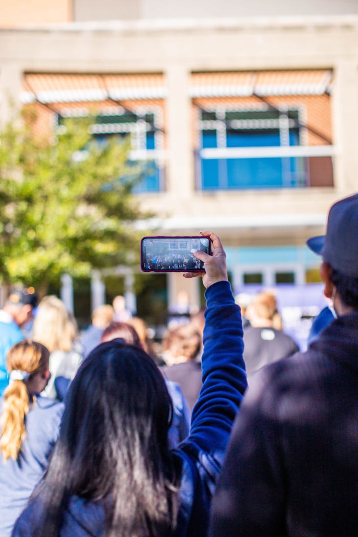 contact-img A crowd gathers, capturing an outdoor event on smartphones with a focus on social media sharing.